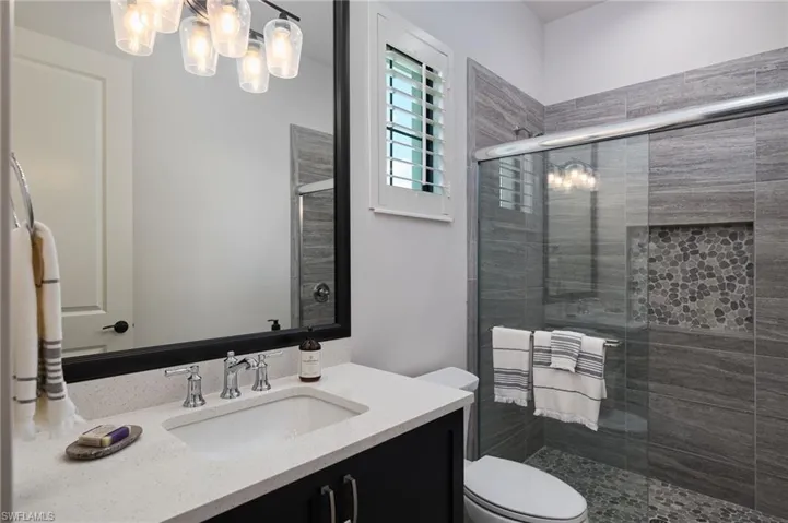 Bathroom with a notable chandelier, vanity, walk in shower, and toilet