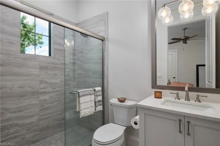 Bathroom with ceiling fan with notable chandelier, a shower with door, vanity, and toilet