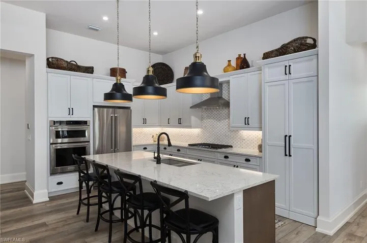 Kitchen featuring sink, wood-type flooring, decorative backsplash, stainless steel appliances, and a center island with sink