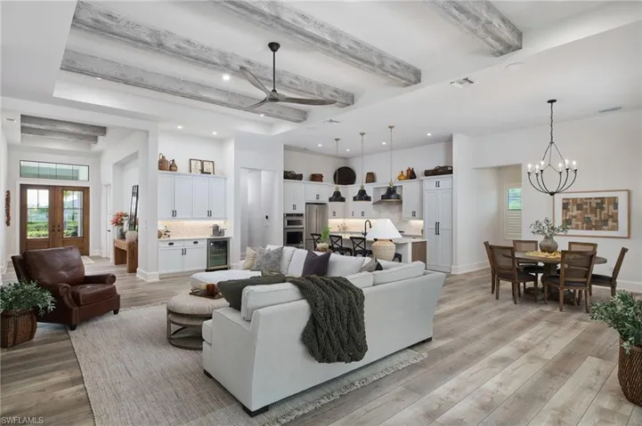 Living room featuring ceiling fan with notable chandelier, beverage cooler, beam ceiling, light hardwood / wood-style floors, and sink