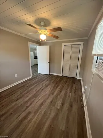 Unfurnished bedroom with ornamental molding, a closet, dark wood-type flooring, a ceiling fan, and wooden ceiling