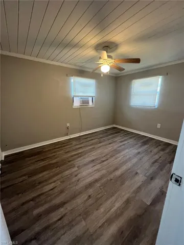 Empty room featuring crown molding, cooling unit, a ceiling fan, wooden ceiling, and dark wood-type flooring