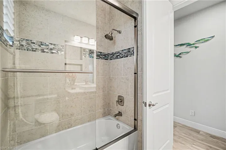 Bathtub with glass shower enclosure, brushed nickel fixtures, tiled surround with decorative mosaic accent.