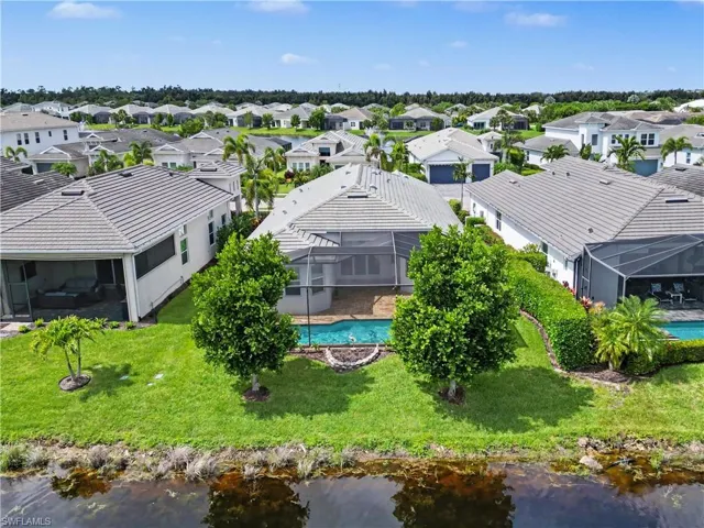Waterfront property with a screened-in pool and covered patio, featuring a tile roof and mature landscaping