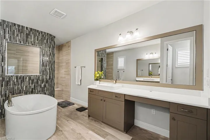 Luxurious primary bath with Freestanding soaking tub, full-height tile accent wall, extensive vanity with dual sinks, and a large wall-mounted mirror