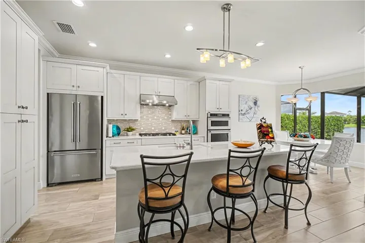 Kitchen featuring white cabinetry, stainless steel Kitchen Aide appliances, a large island with seating, recessed lighting, and upgraded backsplash.