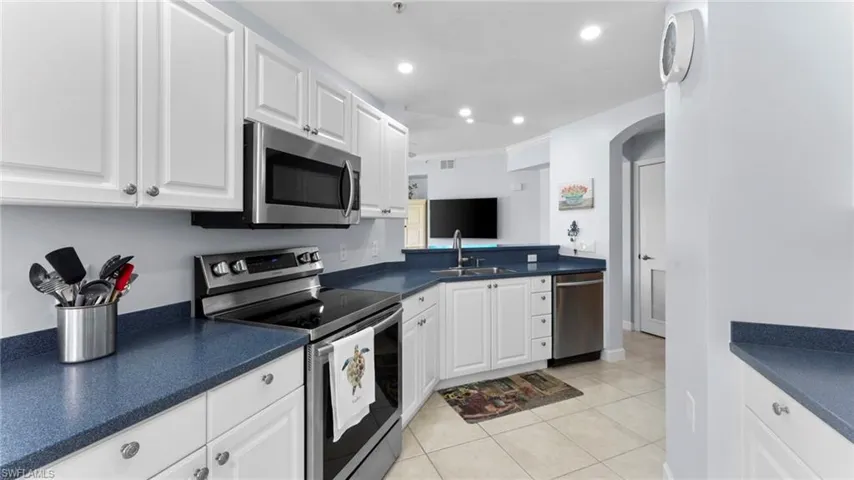 Kitchen with stainless steel appliances, white cabinetry, light tile patterned floors, and sink