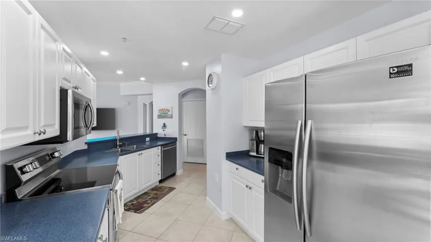 Kitchen featuring sink, light tile patterned floors, stainless steel appliances, and white cabinets