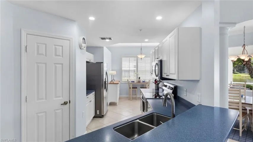 Kitchen with stainless steel appliances, white cabinets, light tile patterned floors, and decorative light fixtures