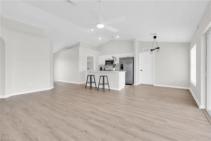Living room with light wood-style flooring, a ceiling fan, arched walkways, and high vaulted ceiling