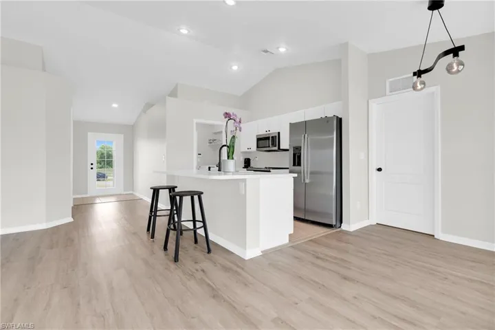 Kitchen featuring appliances with stainless steel finishes, a kitchen bar, light wood-type flooring, an island with sink, and light countertops