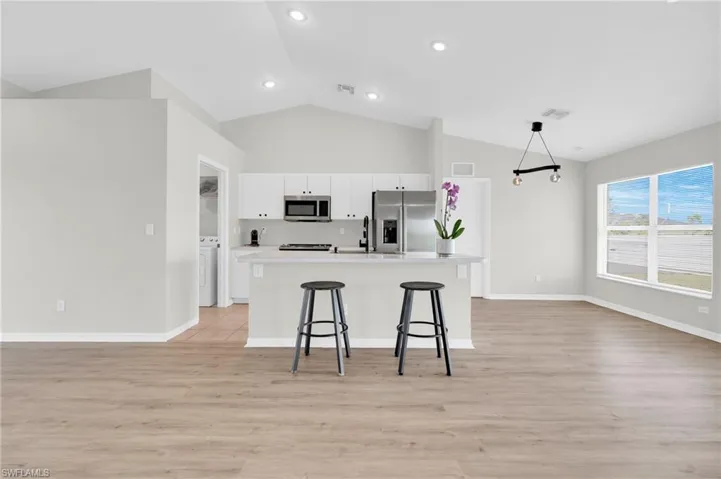 Kitchen featuring stainless steel appliances, white cabinetry, light wood finished floors, a kitchen breakfast bar, and open floor plan