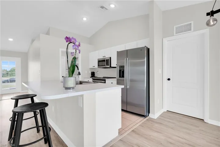 Kitchen featuring stainless steel appliances, a kitchen breakfast bar, lofted ceiling, a kitchen island with sink, and light countertops