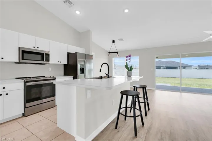 Kitchen featuring stainless steel appliances, white cabinetry, an island with sink, light countertops, and a kitchen breakfast bar