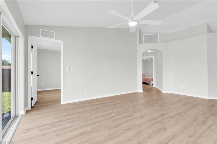 Spare room with plenty of natural light, arched walkways, a ceiling fan, light wood-style floors, and vaulted ceiling