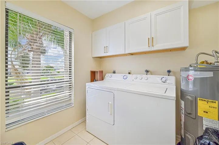 Clothes washing area featuring cabinets, electric water heater, washer and clothes dryer, and light tile patterned floors