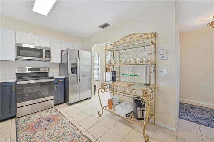 Kitchen with white cabinetry, stainless steel appliances, blue cabinetry, and light tile patterned floors