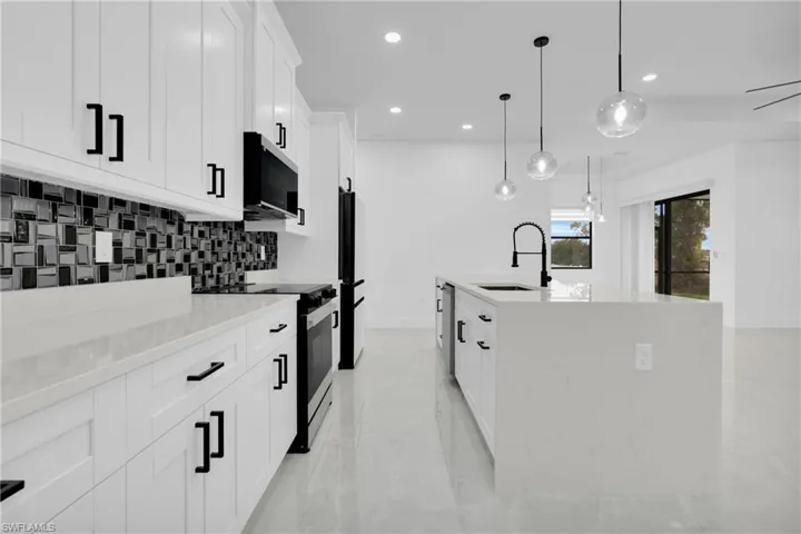 Kitchen featuring electric range, a center island with sink, light stone counters, white cabinetry, and hanging light fixtures