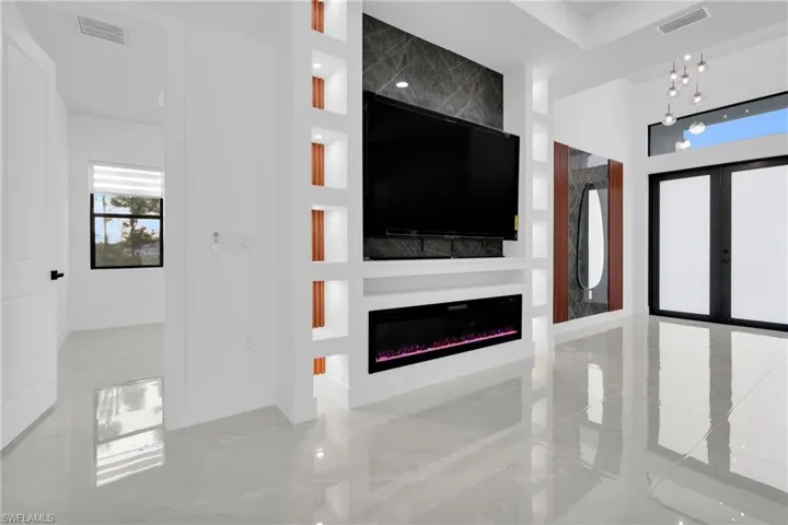 Unfurnished living room with a glass covered fireplace, french doors, light marble finish flooring, and built in shelves