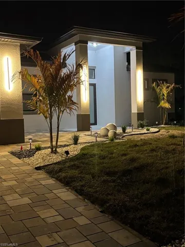 Exterior entry at night with a yard, stucco siding, and covered porch