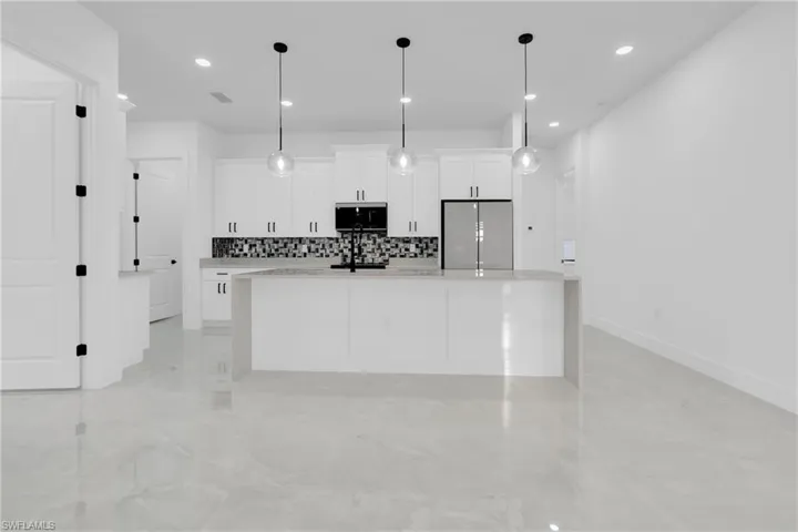 Kitchen with white cabinets, a center island with sink, freestanding refrigerator, and hanging light fixtures
