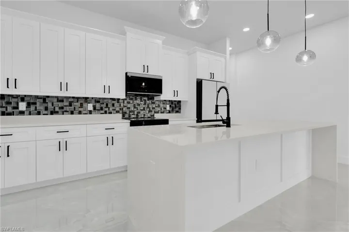 Kitchen featuring white cabinetry, light stone counters, pendant lighting, an island with sink, and decorative backsplash