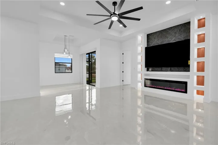 Unfurnished living room with a large fireplace, a raised ceiling, built in features, a ceiling fan, and recessed lighting