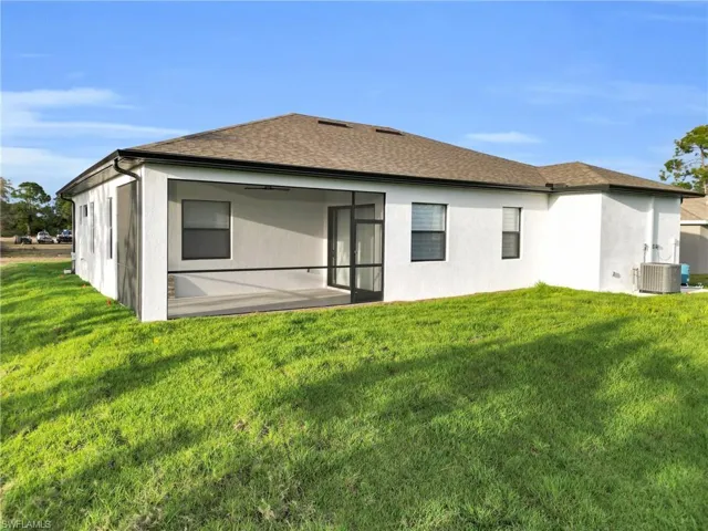 Back of property with stucco siding, a yard, and roof with shingles