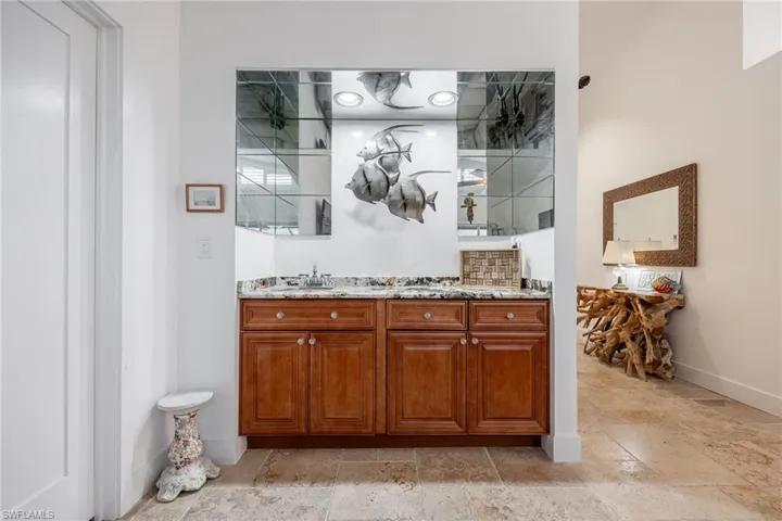 Mirrored wet bar featuring light stone counters and sink