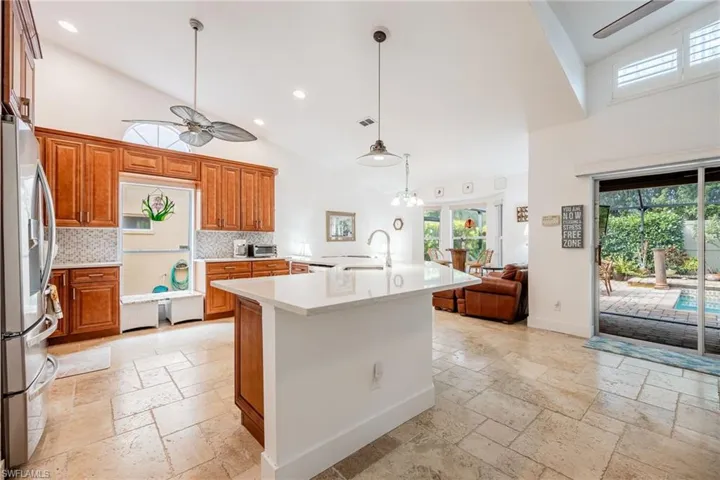 Kitchen with stainless steel refrigerator with ice dispenser, sink, high vaulted ceiling, an island with sink, and backsplash