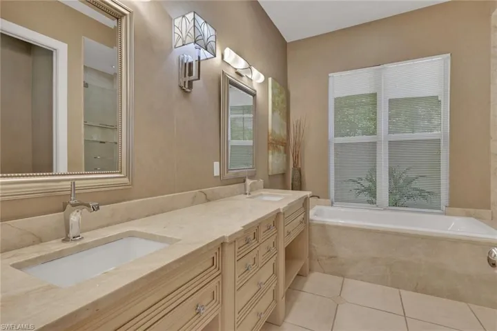Bathroom with double vanity, light tile patterned flooring, and a bath