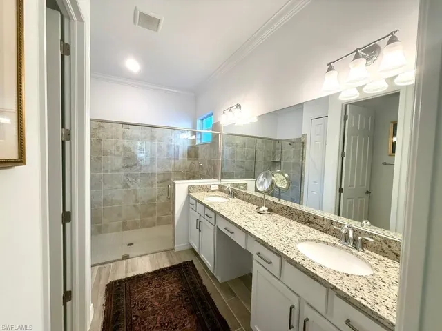 Full bathroom with a stall shower, double vanity, ornamental molding, and light wood-style flooring
