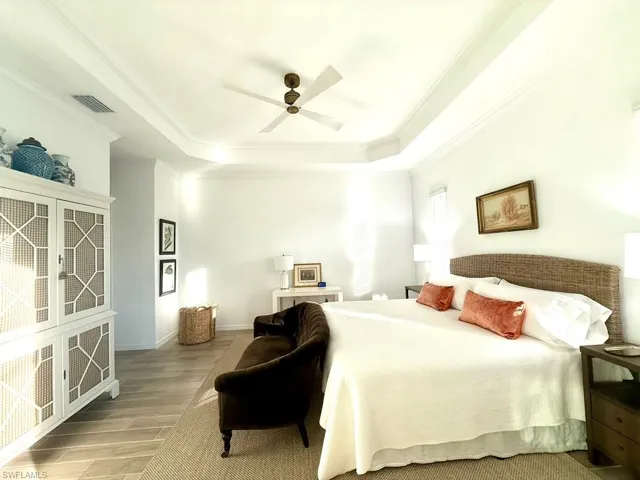 Bedroom with light wood finished floors, a raised ceiling, crown molding, and ceiling fan