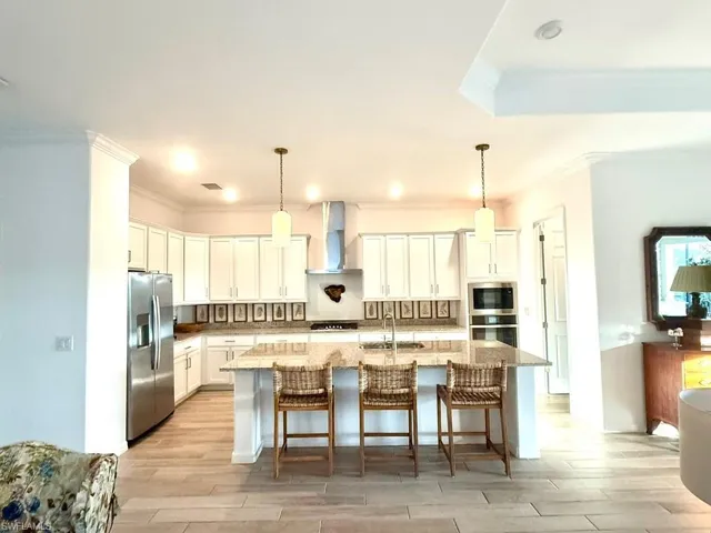 Kitchen featuring a kitchen breakfast bar, ornamental molding, appliances with stainless steel finishes, white cabinets, and an island with sink
