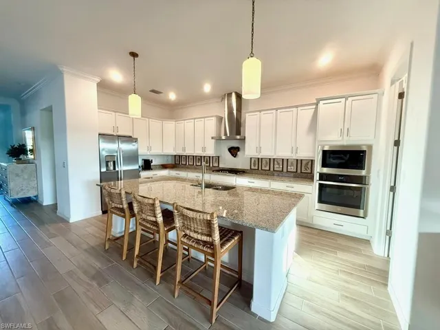 Kitchen featuring light stone countertops, wood finish floors, white cabinets, a kitchen breakfast bar, and appliances with stainless steel finishes