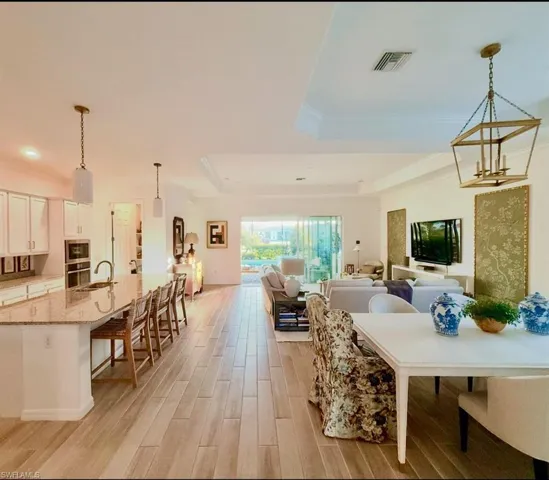 Dining area with a raised ceiling, light wood-style flooring, and ornamental molding