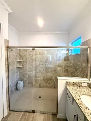 Full bathroom with light wood finished floors, a stall shower, crown molding, and vanity