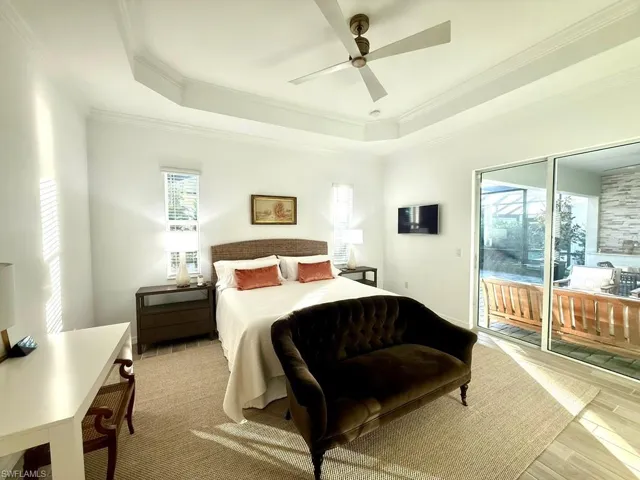Bedroom featuring a tray ceiling, crown molding, access to outside, a ceiling fan, and light wood finished floors