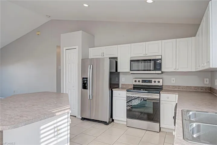 Kitchen with stainless steel appliances, lofted ceiling, white cabinetry, light countertops, and light tile patterned floors