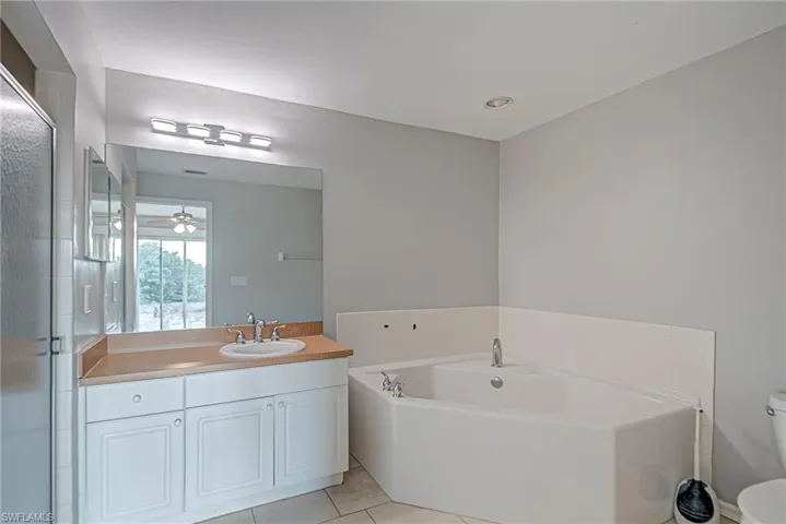 Full bath featuring vanity, a bath, light tile patterned flooring, and ceiling fan