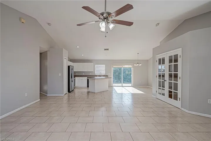 Unfurnished living room with ceiling fan, french doors, lofted ceiling, hanging lights, and light tile patterned flooring
