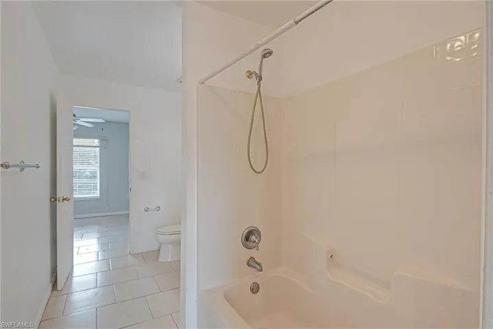 Bathroom with bathtub / shower combination, light tile patterned floors, and a ceiling fan