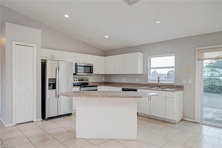 Kitchen with stainless steel appliances, white cabinets, a kitchen island, vaulted ceiling, and light countertops