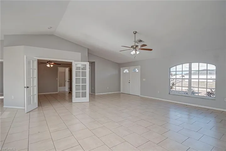 Unfurnished living room featuring french doors, a ceiling fan, vaulted ceiling, and light tile patterned floors