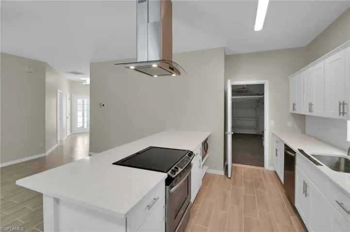 Kitchen featuring stainless steel appliances, island range hood, light stone counters, light colored carpet, and white cabinetry