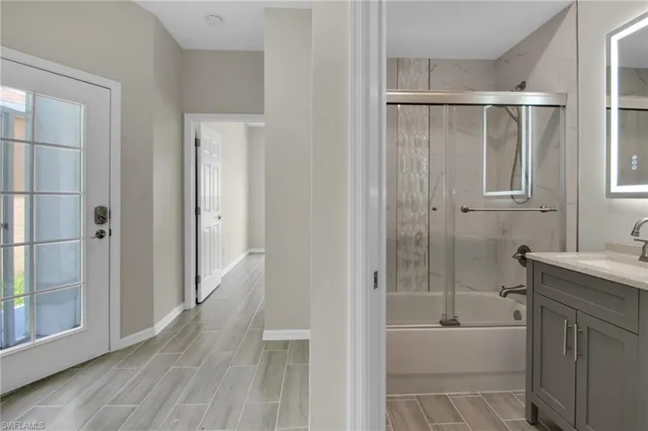 Bathroom with bath / shower combo with glass door and vanity