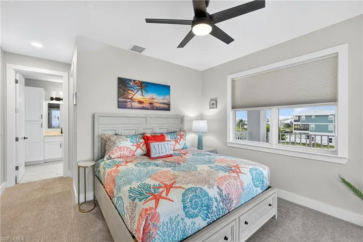Bedroom featuring a ceiling fan, ensuite bathroom, and light colored carpet - Virtually Edited Image