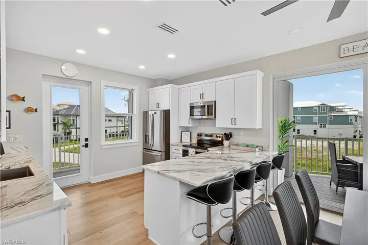 Kitchen with light stone countertops, a kitchen bar, stainless steel appliances, white cabinets, and recessed lighting - Virtually Edited Image