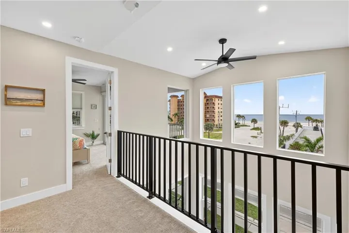 Hallway featuring a water view, healthy amount of natural light, light carpet, recessed lighting, and lofted ceiling - Virtually Edited Image