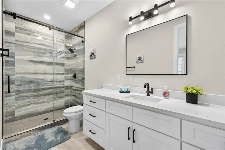 Full bathroom featuring vanity, a stall shower, and light wood finished floors - Virtually Edited Image